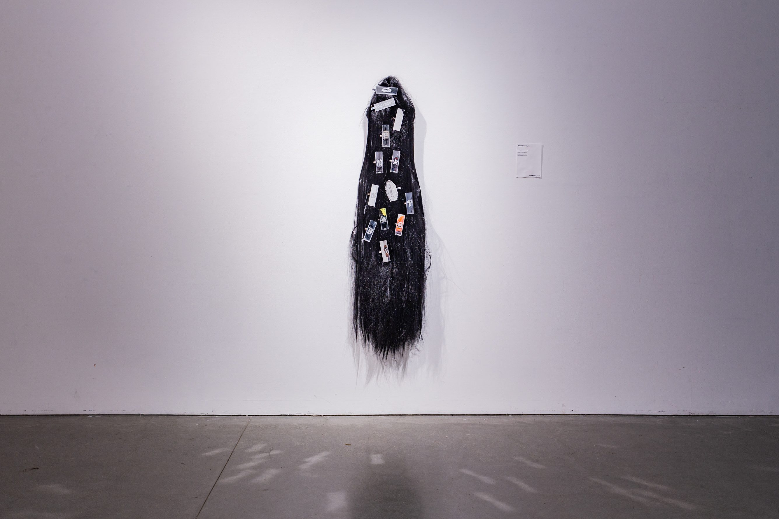 A black wig with various clips made of acrylic on it, displayed against a white wall.